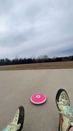 a person standing next to a pink frisbee on top of a cement ground