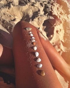 a woman laying on top of a sandy beach next to the ocean with shells all over her body