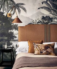 a bed with two lamps hanging from the headboard and palm trees on the wall behind it