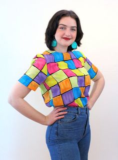 This is a sweet colorful 90s vintage "Notations" top! It's a bright color block geometric square print in shades of pink, blue, yellow, purple and orange with black grid lines. A short sleeved pullover, it has a boxy shape, a high round neckline, no shoulder pads, and it closes with a back keyhole neckline and a black button and loop. The fabric is a lightweight silken polyester.This top is in very good clean vintage condition, no flaws noted. The label says "Notations, Size S, 100% Polyester, M Retro Multicolor Tops With Rainbow Print, Retro Multicolor Rainbow Print Top, Retro Multicolor Top With Geometric Pattern, Fitted Retro Multicolor Tops, Retro Multicolor Tops With Retro Print, Retro Spring Top With Rainbow Print, Retro Blue Top With Colorful Pattern, Multicolor Retro Print Tops, Retro Rainbow Print Top For Spring