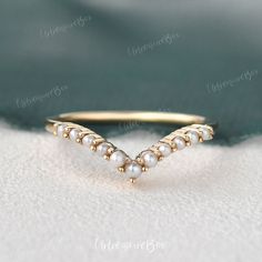 a gold ring with pearls on it sitting on top of a white cloth covered surface