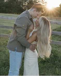 a man and woman kissing in front of a fence with the sun setting behind them