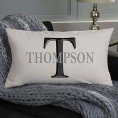 a throw pillow with the letter t on it sitting on a chair next to a lamp