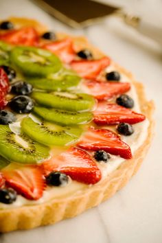 a fruit pizza is topped with kiwis, strawberries and blueberries on top