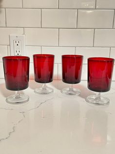 four red glasses sitting on top of a white counter next to a light switch box