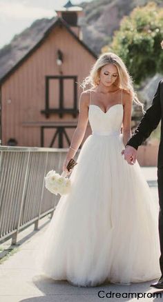 a bride and groom walking down the street holding hands with each other in front of a barn