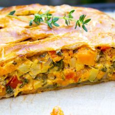 a vegetable quiche is cut into pieces on a piece of parchment paper with a sprig of thyle