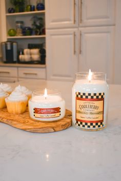 two cupcakes on a cutting board next to a candle in a glass jar