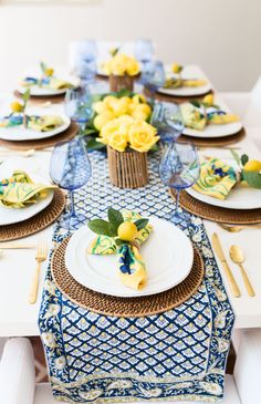 the table is set with yellow flowers and blue napkins, plates and utensils