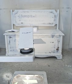 an old white bench sitting in the middle of a cement floor next to a trash can