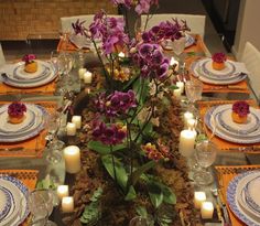 the table is set with plates, candles and purple orchids in vases on it