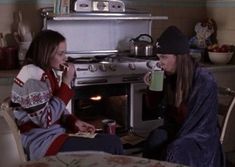 two women are sitting in front of an oven and one is holding a coffee cup