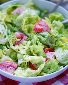 a salad with lettuce and tomatoes in a white bowl on a checkered table cloth