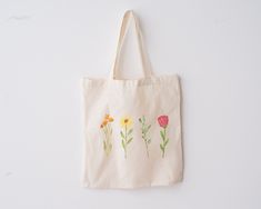 a tote bag with flowers painted on the front and side, hanging from a wall