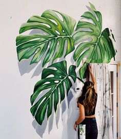 a woman painting a palm leaf on the wall