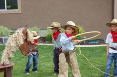 four children in cowboy hats are playing with a toy horse and lasso on the lawn