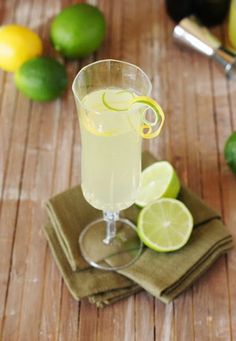 a glass filled with lemonade sitting on top of a wooden table next to limes