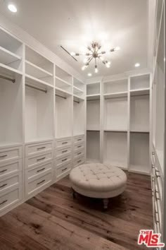 an empty walk - in closet with white cabinets and drawers, including a footstool