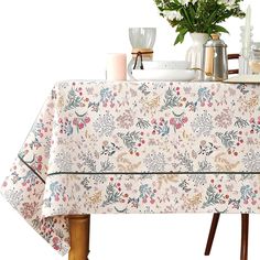 a table with a flowered cloth on it next to some vases and candles