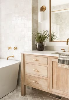 a white bath tub sitting next to a wooden sink vanity in a bathroom under a mirror