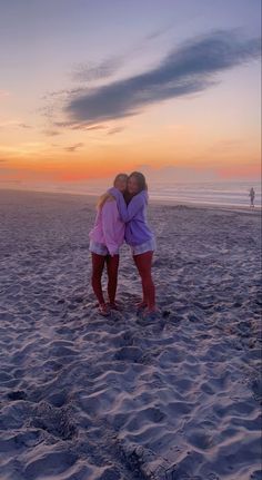 two girls hugging on the beach at sunset with their arms around each other as they stand in the sand