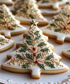 decorated cookies on a white plate with gold trimmings and holly tree decorations,