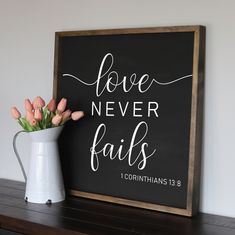 a chalkboard sign with the words love never falls and flowers in a white vase