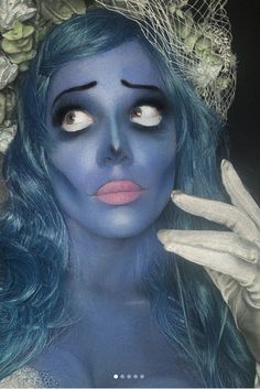 a woman with blue hair and makeup is holding her hand up to her face while wearing white gloves