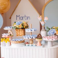 there are many desserts on the table with blue and yellow balloons in the background