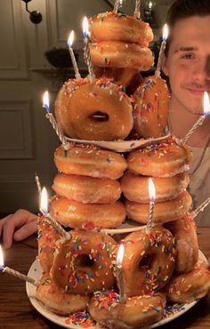 a man sitting in front of a stack of doughnuts with candles on them