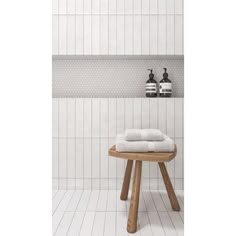 a wooden stool sitting in front of a white tiled shower stall with two soap dispensers