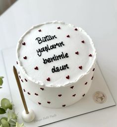 a white cake with writing on it sitting on top of a table next to a potted plant