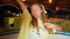 a woman is smiling and holding her arms up in the air at an amusement park