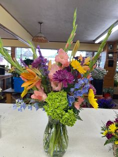 a vase filled with lots of colorful flowers on top of a white tablecloth covered table