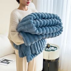 a woman holding a pile of blue towels in front of a white couch and window