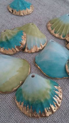 four blue and green seashells sitting on top of a gray cloth covered floor