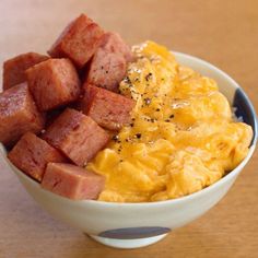 a white bowl filled with breakfast food on top of a wooden table next to a fork