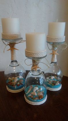 three glass vases with seas in them sitting on a wooden table next to two white candles