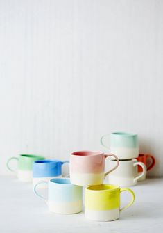 four different colored coffee mugs sitting next to each other on a white counter top