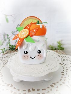 a small ceramic cup with an orange on it's head sitting on top of a doily