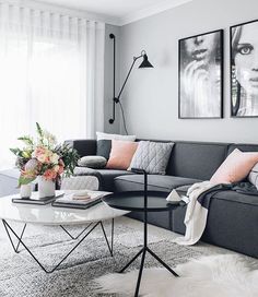 a living room with grey couches and pink pillows on the table in front of two pictures