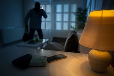 a person in a dark room with a cell phone on a table next to a lamp