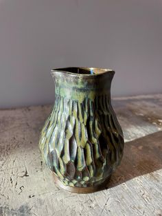 a green vase sitting on top of a wooden table next to a wall and floor