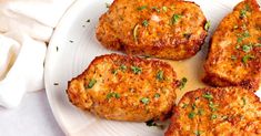 four meat patties on a white plate with sauce and parsley sprinkled