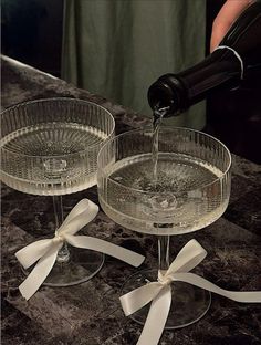 someone pouring wine into two glasses on top of a marble counter with white ribbons and bows