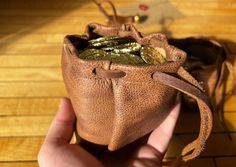 a hand holding a small brown purse on top of a wooden floor