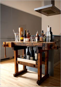 a wooden table topped with lots of bottles and glasses next to a stove top oven