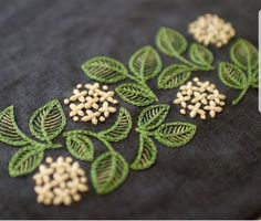 some green leaves and white flowers are on a black fabric piece with thread work in the middle