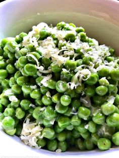 a white bowl filled with green peas covered in shredded parmesan cheese