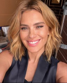 a woman with blonde hair and blue eyes smiles at the camera while sitting in a chair